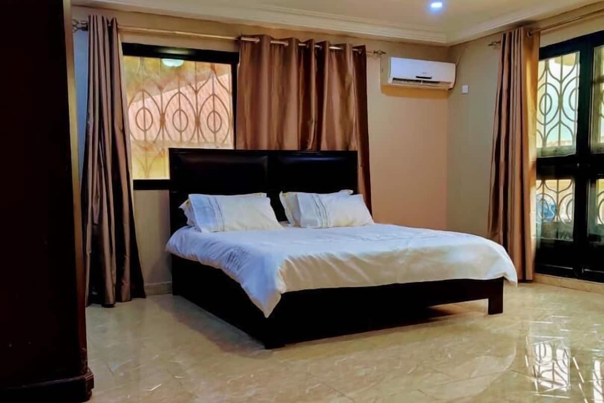 A bedroom with a large bed, a ceiling light, and a window with curtains.