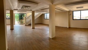 A spacious room with wooden flooring, large windows, and a staircase leading to another level. - Nimi Beach Resort (Freetown)
