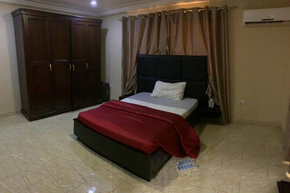 A bedroom with a bed, a wardrobe, curtains, and an air conditioning unit.