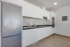 Enjoy cooking in this well-lit kitchen with a stainless steel refrigerator, microwave, and oven.