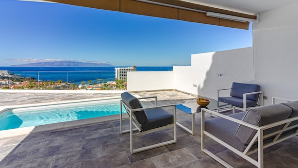 A balcony with a pool, two chairs, and a table.