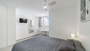 A bedroom with a bed, a desk, a chair, a TV, and a ceiling fan.