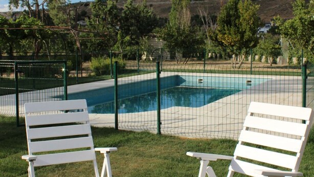 A swimming pool with a net fence, surrounded by white chairs and greenery. - Rural house viaverde del Tajuña (Perales de Tajuña)