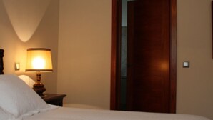 A bedroom with a bed, a nightstand with a lamp, and a wooden door. - Rural house viaverde del Tajuña (Perales de Tajuña)