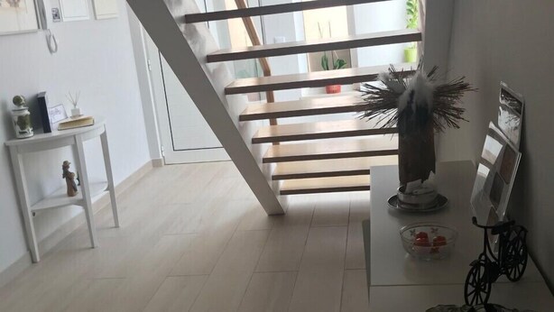 Eine Treppe mit Holzbalken, eine weiße Wand mit gerahmten Bildern, ein kleiner Tisch mit Dekoration und eine Glas-Schale mit Pralinen.