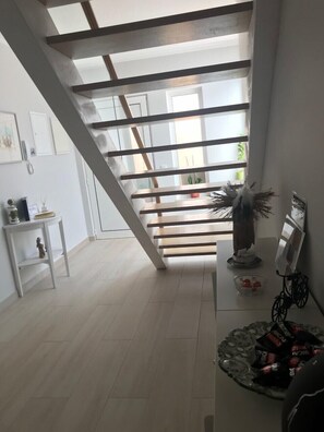 Una escalera con vigas de madera, una pared blanca con cuadros enmarcados, una mesita con adornos y un bol de cristal con bombones.