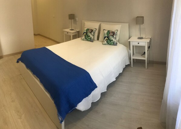 Un dormitorio con una cama, dos mesitas de noche y una colcha azul.