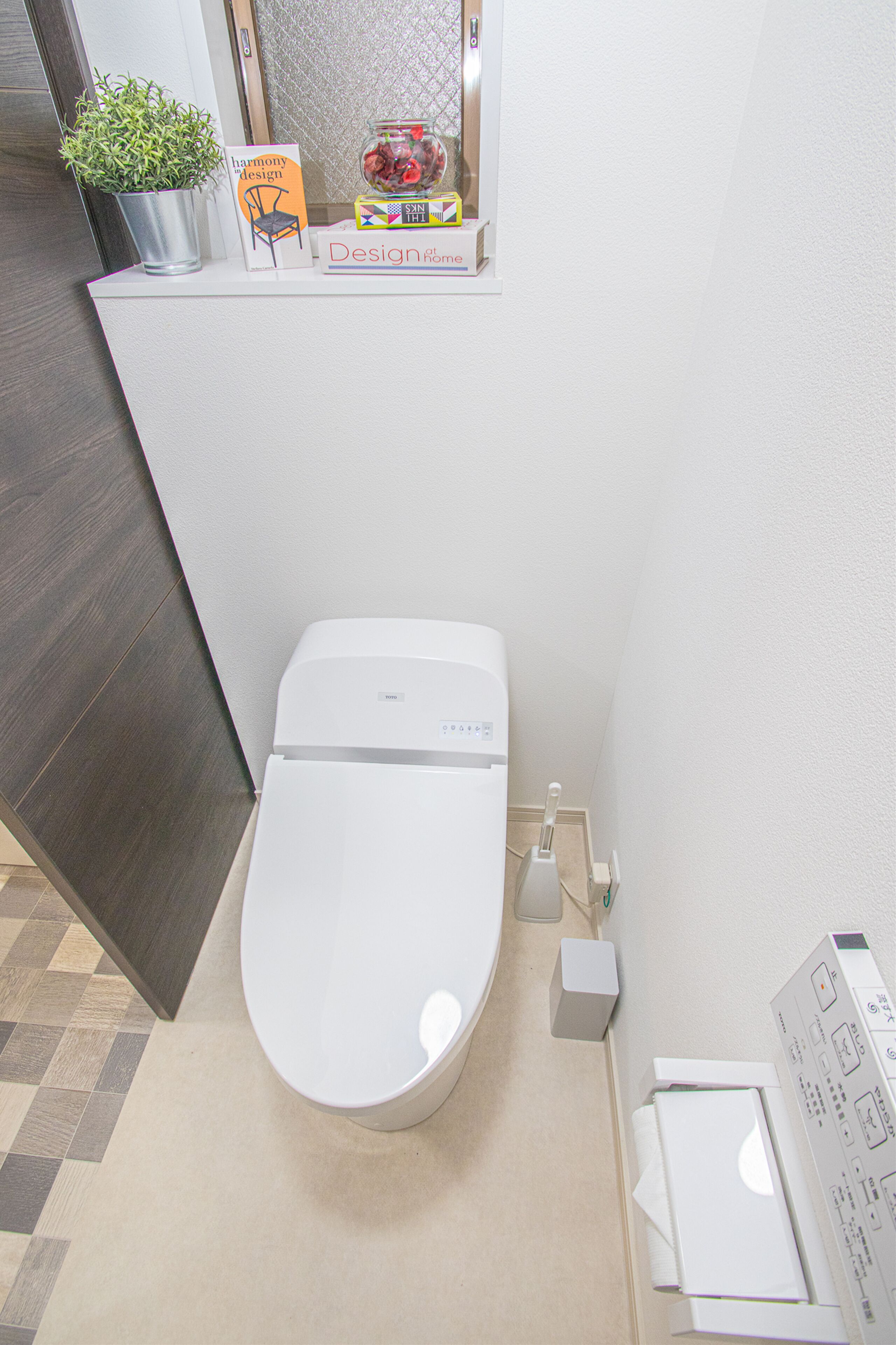 A modern bathroom with a white toilet, a potted plant, a Harmony Design book, and a decorative jar.