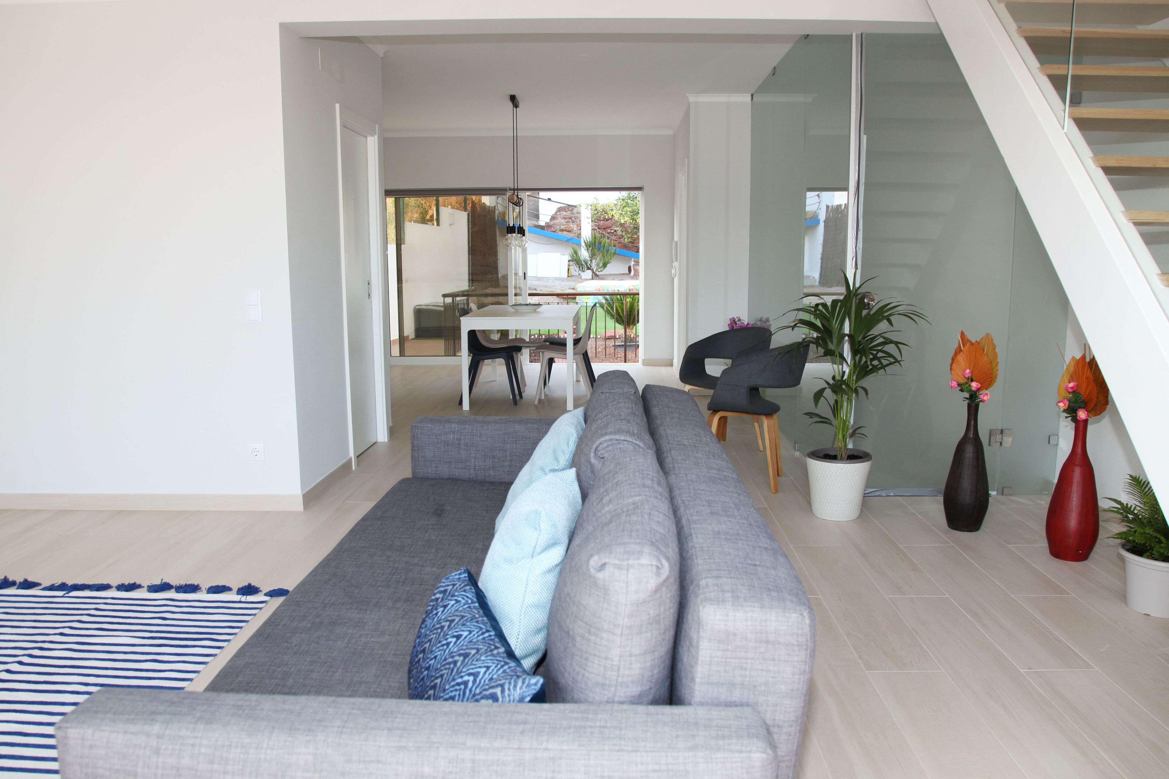 Ein modernes Wohnzimmer mit grauem Sofa, einem Streifen Teppich und einer Treppe, die in einen oberen Bereich führt.