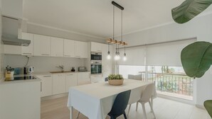 Une cuisine moderne avec des meubles blancs, un coin repas comprenant une table et des chaises, et une grande fenêtre offrant une belle vue.
