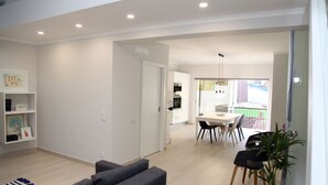 Un salon moderne avec un canapé gris, un coin repas avec une table et des chaises, et une cuisine en arrière-plan.