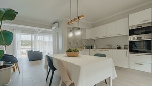Une cuisine moderne avec des meubles blancs, une table à manger avec des chaises et un luminaire suspendu.
