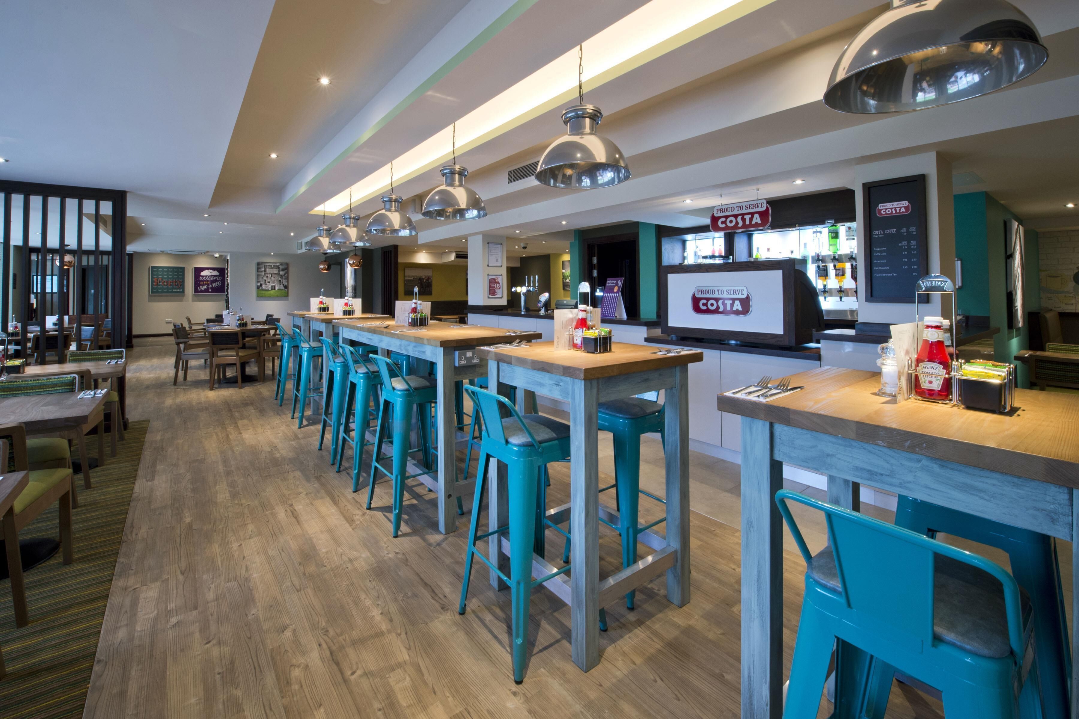 Un área de bar moderna con taburetes de color turquesa, una barra de madera e iluminación colgante.