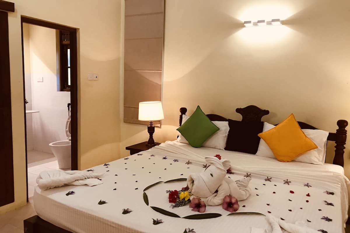 A neatly made bed with floral bedding, a bedside lamp, and a towel on the floor.