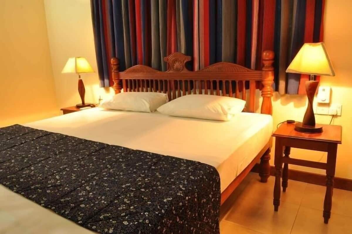 A hotel room with a bed, two bedside lamps, a wooden headboard, and a striped curtain backdrop.