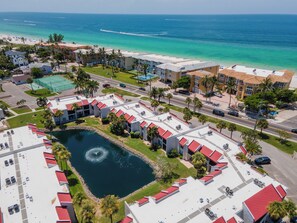 An aerial view of a coastal hotel with a central courtyard, a swimming pool, and a beach view.