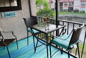 A balcony with a glass table and chairs, a sign reading "Towels", and a view of a building and greenery.