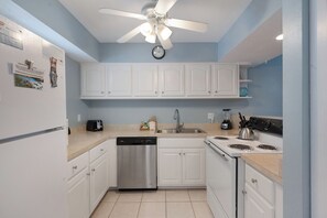 Une cuisine avec des armoires blanches, un lave-vaisselle en acier inoxydable, une cuisinière à quatre brûleurs et un ventilateur de plafond.