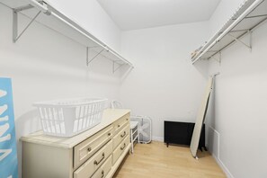 A small, well-lit room with a wooden floor, a white dresser with drawers, a white basket on top, and a white fan.