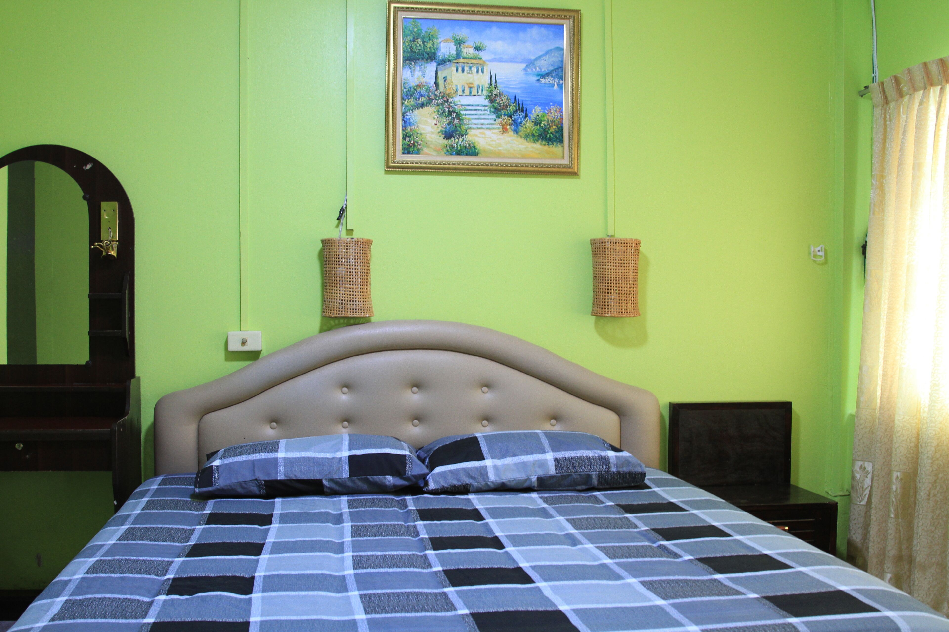 A bedroom with a bed, a headboard, a painting on the wall, and a mirror.