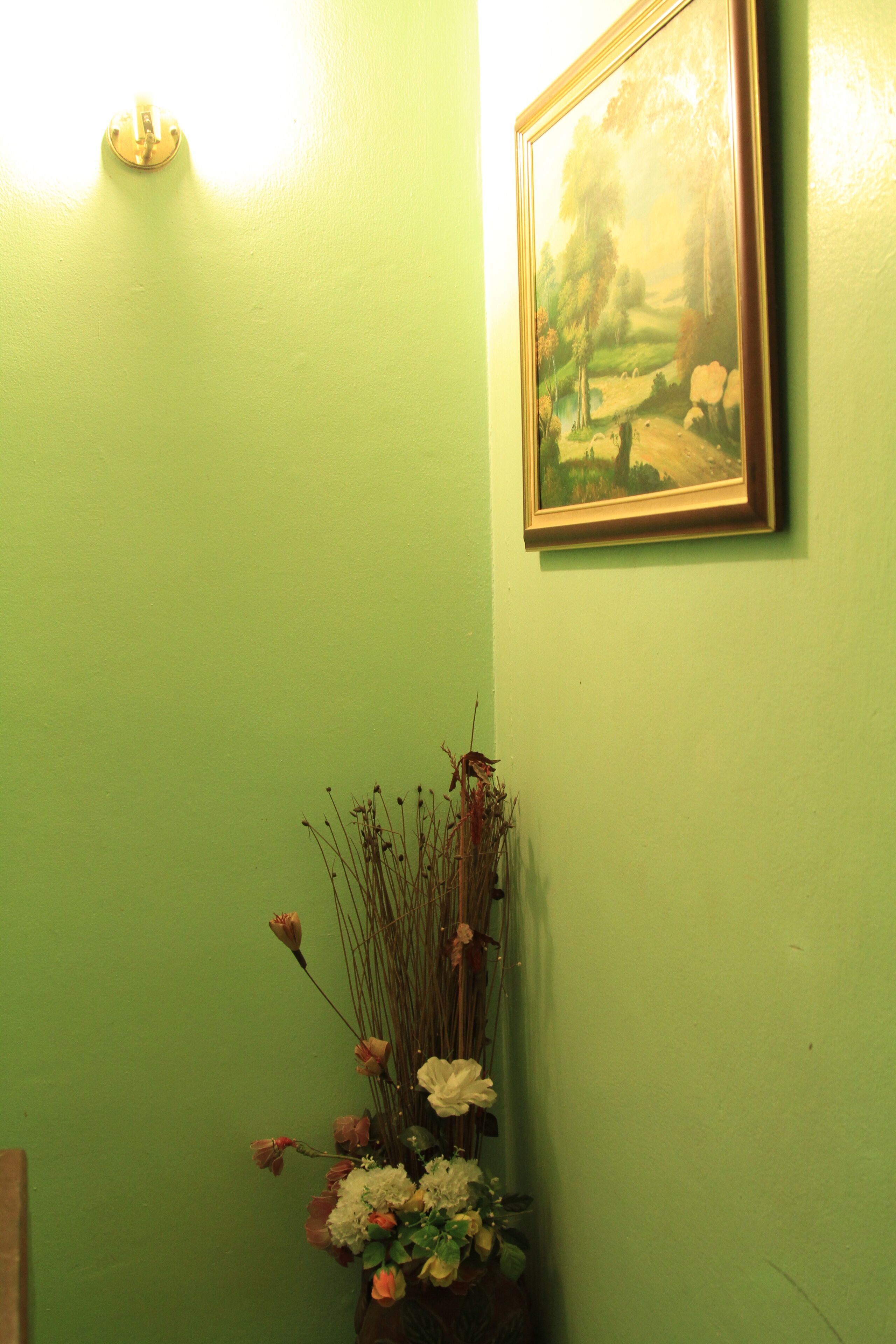 A room with a green wall, a framed painting, and a vase of flowers.