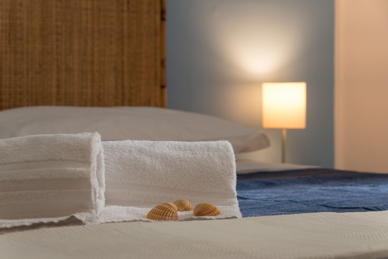 Un lit bien fait, avec une serviette blanche pliée et trois coquillages disposés sur une couverture bleue.