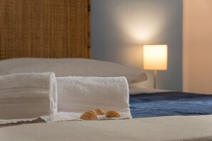 Una cama bien hecha con una toalla blanca doblada y tres conchas marinas sobre una colcha azul.
