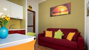 Ein Wohnzimmer mit einem roten Sofa, einer blauen Vase mit Blumen und einem Gemälde, das einen Sonnenuntergang zeigt.