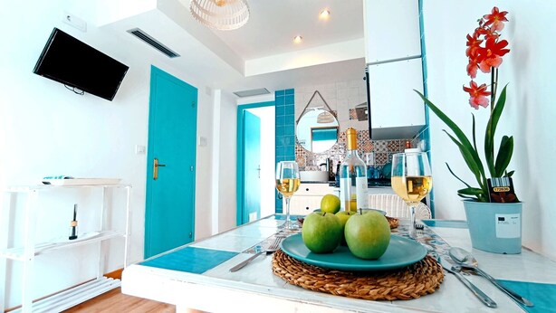 A modern kitchen with a dining area, featuring a teal door, a flat-screen TV, and a potted plant. - Casas del Castillo de Peñíscola EGVT-498-CS - Deluxe Apartment (Peñíscola)