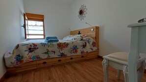 A bedroom with a wooden bed, a small bedside table, a chair, a window with blinds, and a wall decoration. - Casas del Castillo de Peñíscola EGVT-498-CS - Deluxe Apartment (Peñíscola)