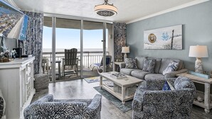 A spacious living area with a balcony, a sofa set, patterned armchairs, a coffee table, and a painting on the wall. - 0209 Waters Edge Resort 1 Bedroom Condo by RedAwning (Murrells Inlet)