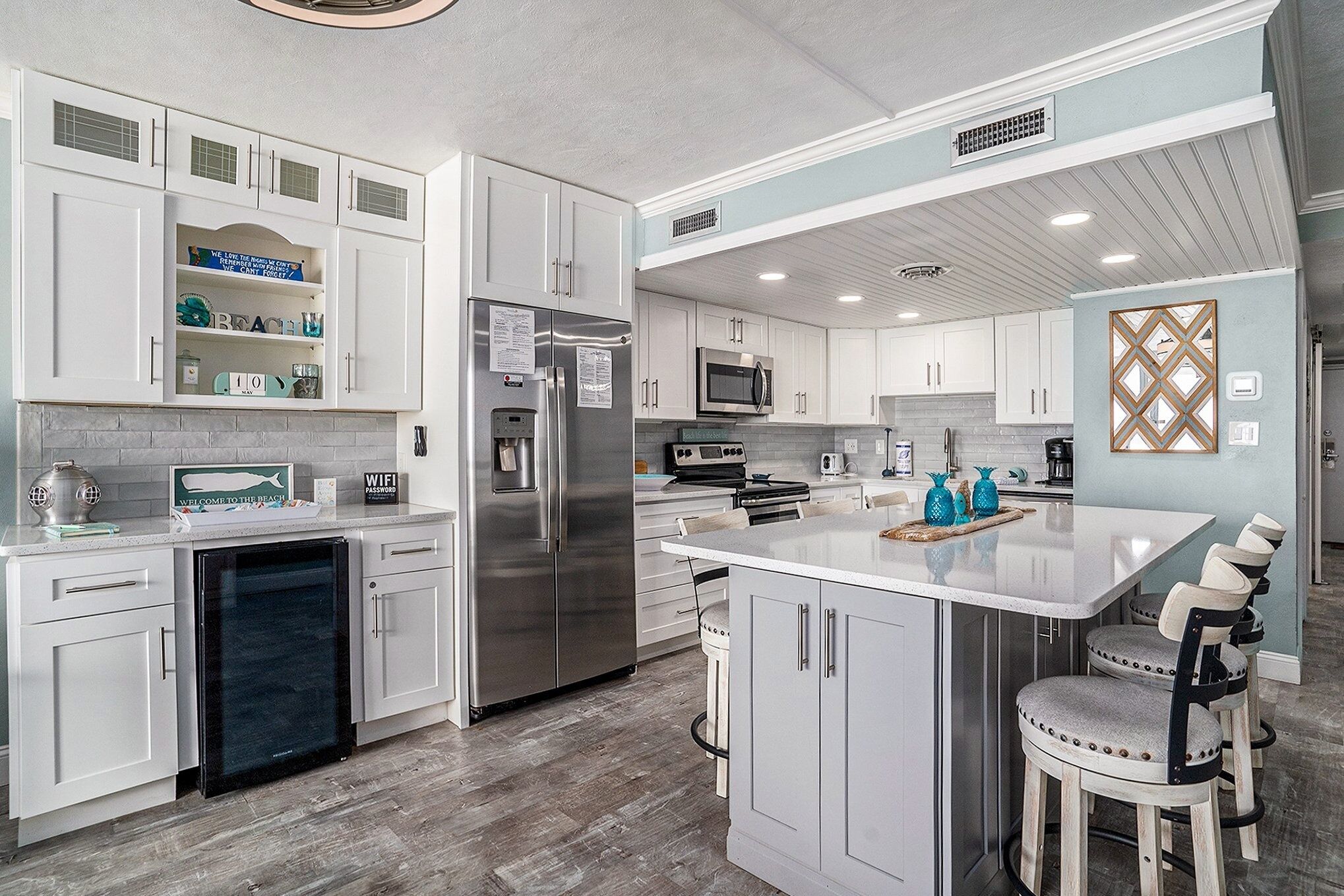 A modern kitchen with white cabinetry, stainless steel appliances, and a central island with bar stools.