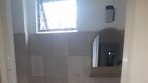 A small bathroom with a toilet, a sink, and a window. - Oasis Inn (Negombo)