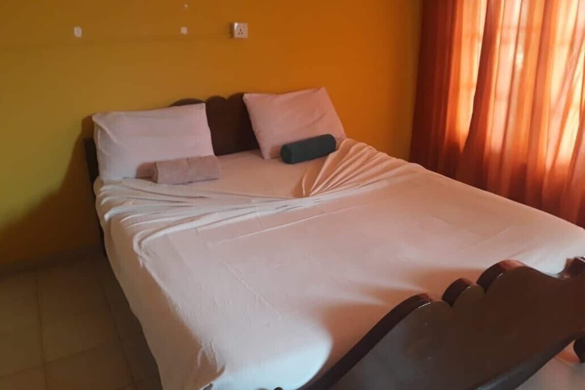 Una cama bien hecha con almohadas y una colcha, cabecera y una ventana con cortinas.