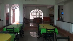 A dining area with tables and chairs, a ceiling fan, and a view through an arched doorway. - Oasis Inn (Negombo)