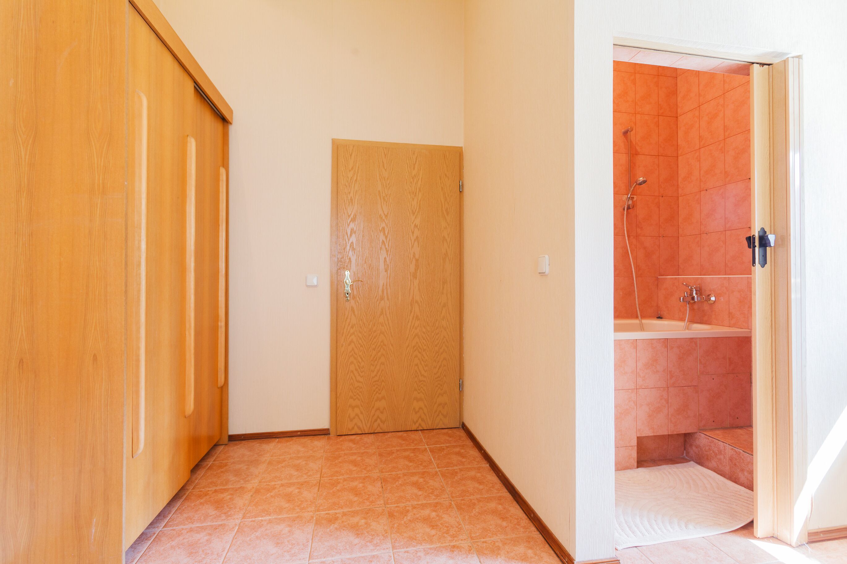 Een gang met een houten deur en een badkamer met oranje tegels en een douche.