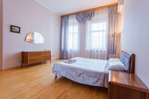 Quarto com cama, penteadeira de madeira, espelho e janela com cortinas.