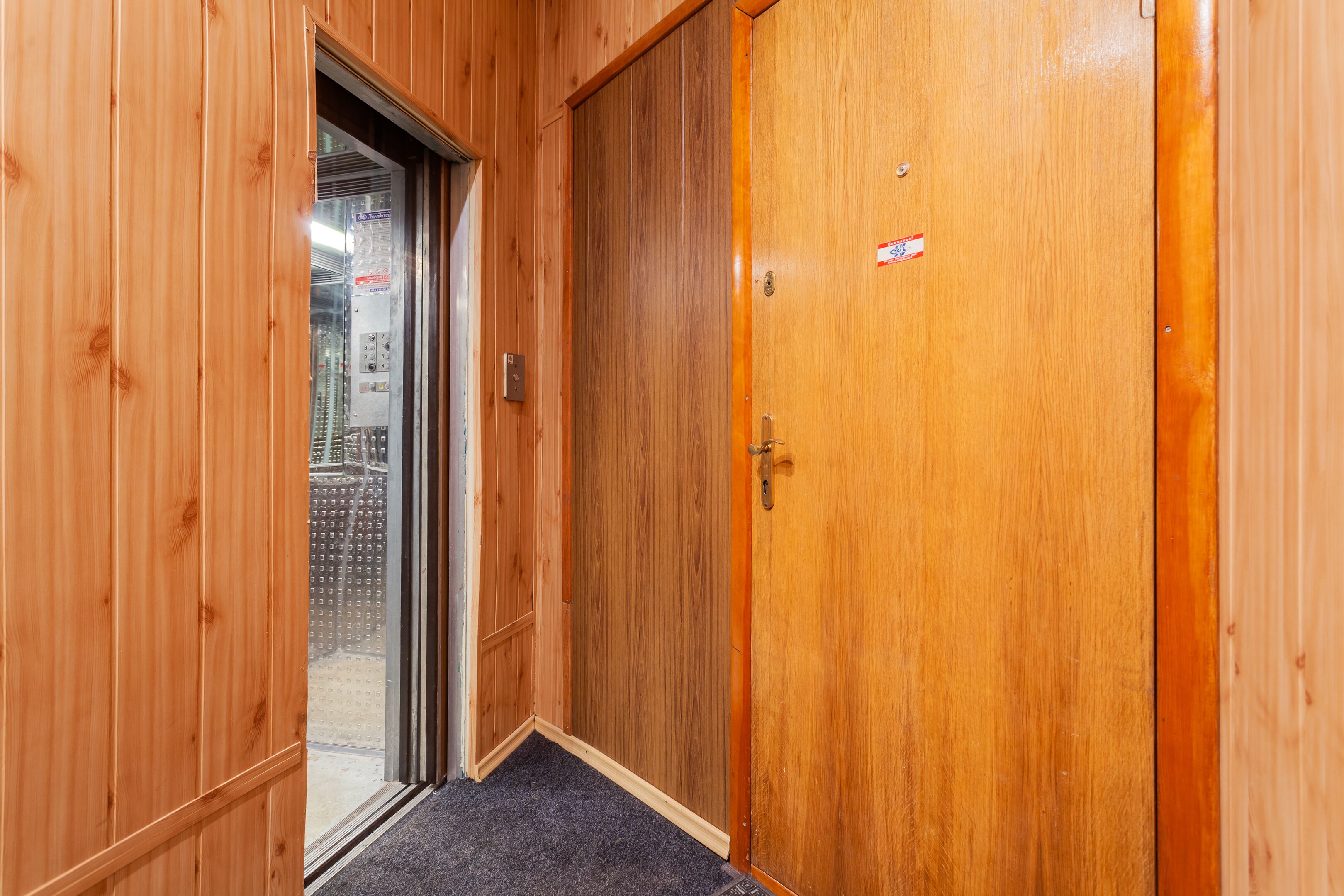 Um corredor de madeira com uma porta que dá para um quarto com piso coberto de carpete.