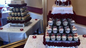 Une présentation de desserts à plusieurs niveaux, comprenant des cupcakes et un gâteau de mariage, décoré de roses et surmonté d’un cœur.