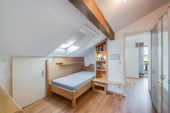 A small, well-lit room with a sloped ceiling, a single bed, a wooden desk, and a bookshelf. - Alpenblick, apartment with terrace and balcony (Eggstätt)