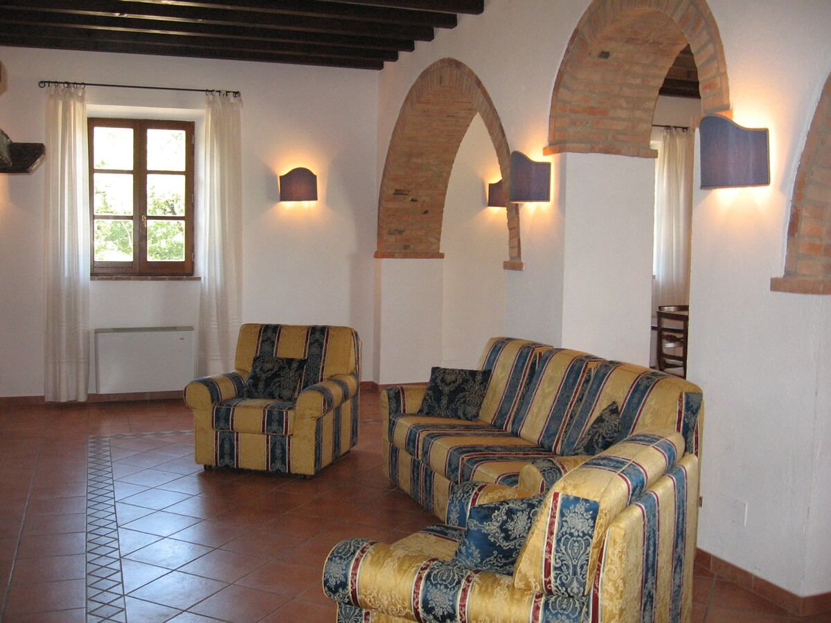Una sala de estar con dos sillones y un sofá, una ventana con cortinas y arcos de ladrillo en las paredes.