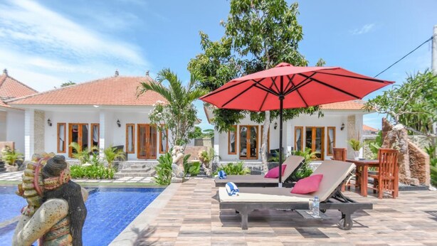 A poolside area with lounge chairs and a red umbrella, surrounded by a tiled patio and greenery. - Adi Abian Villas (Pecatu)
