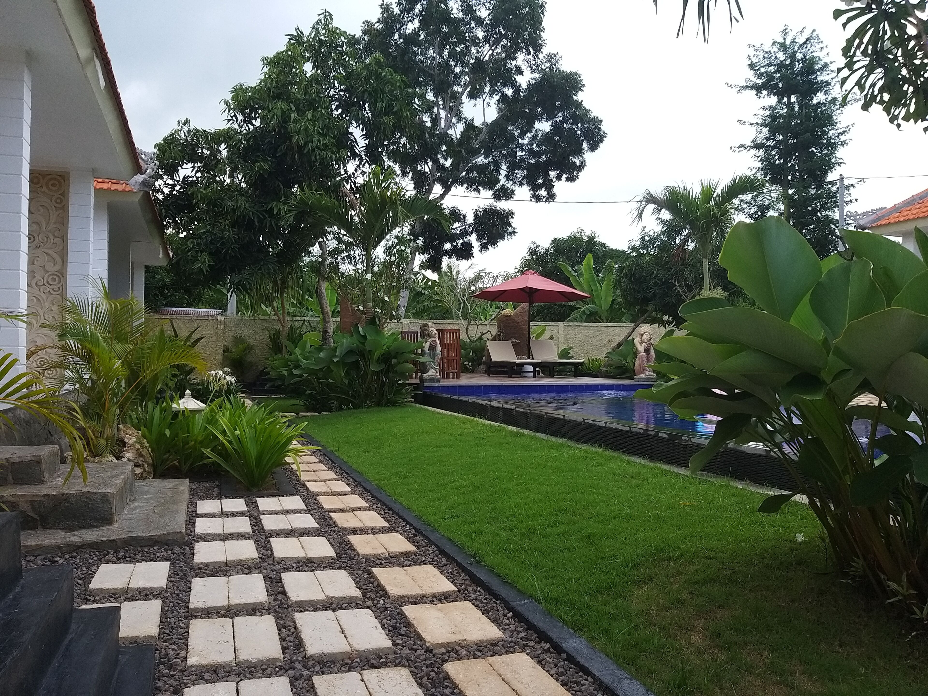 A garden with a swimming pool, a red umbrella, and a statue.