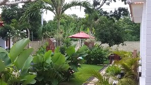 A garden with a paved pathway, large green plants, and a red umbrella. - Adi Abian Villas (Pecatu)