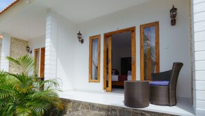 A covered outdoor area with a wicker chair and a small table, a wooden door leading to a bedroom, and a stone wall. - Adi Abian Villas (Pecatu)