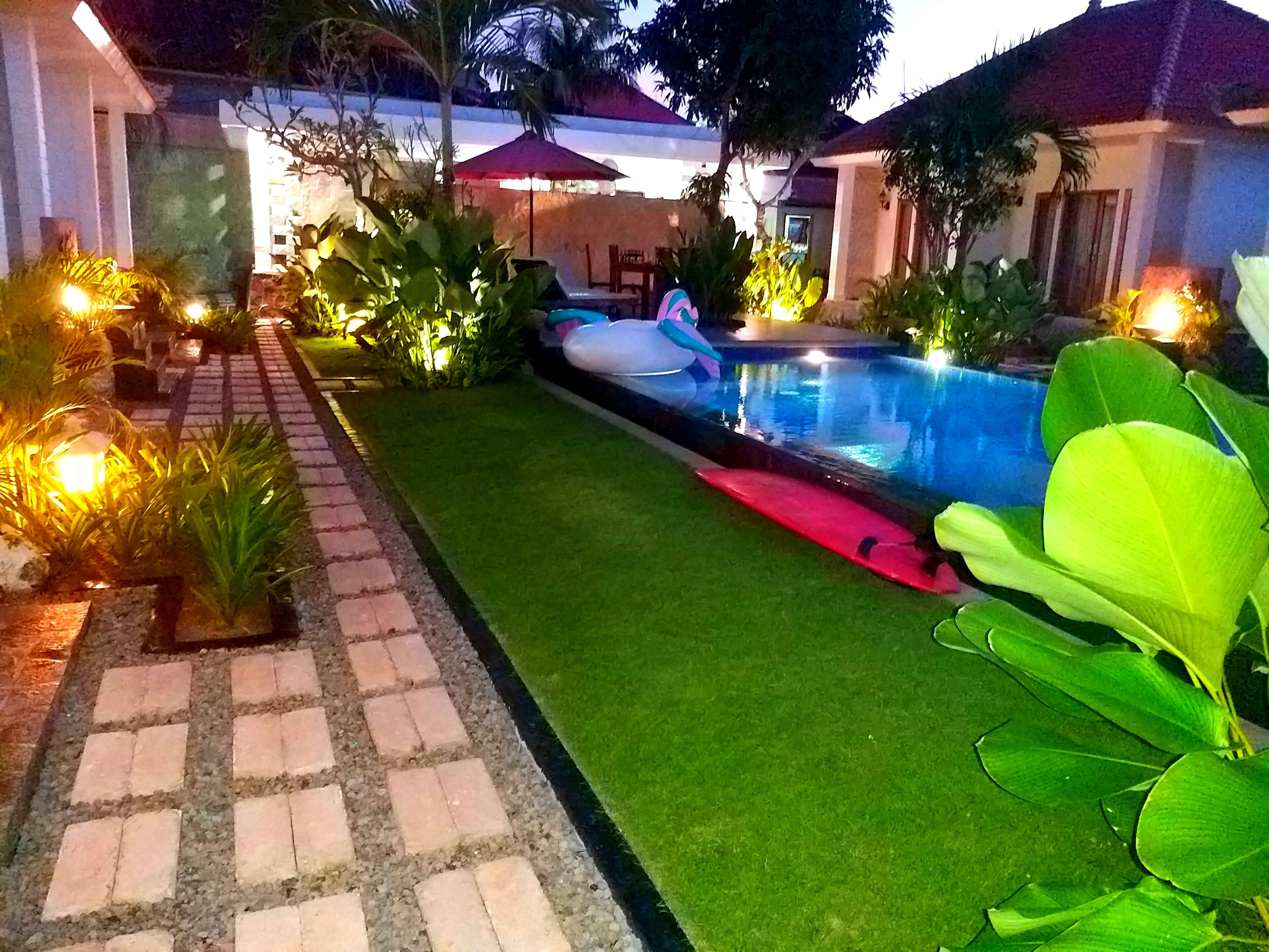 A swimming pool with a red surfboard, surrounded by well-maintained grass and plants.
