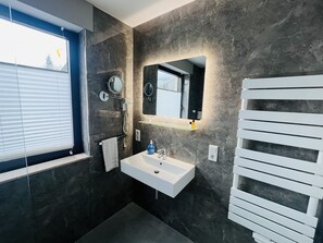 Een moderne badkamer met een witte wastafel, een spiegel en een handdoekhouder.