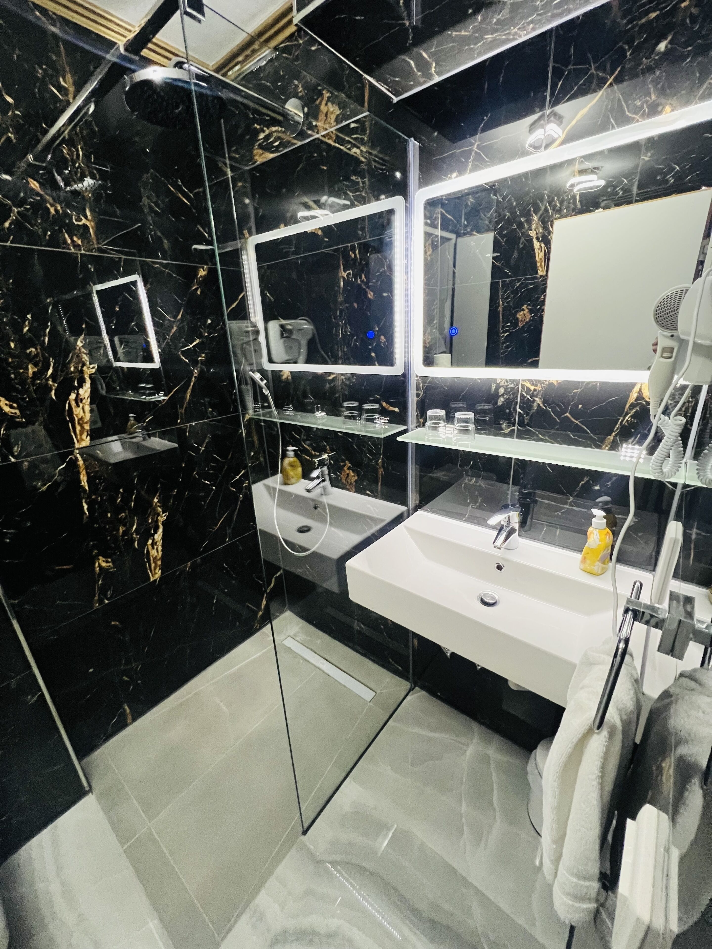 Une salle de bain moderne avec un mur en marbre noir, un lavabo blanc, un miroir et un sèche-cheveux.
