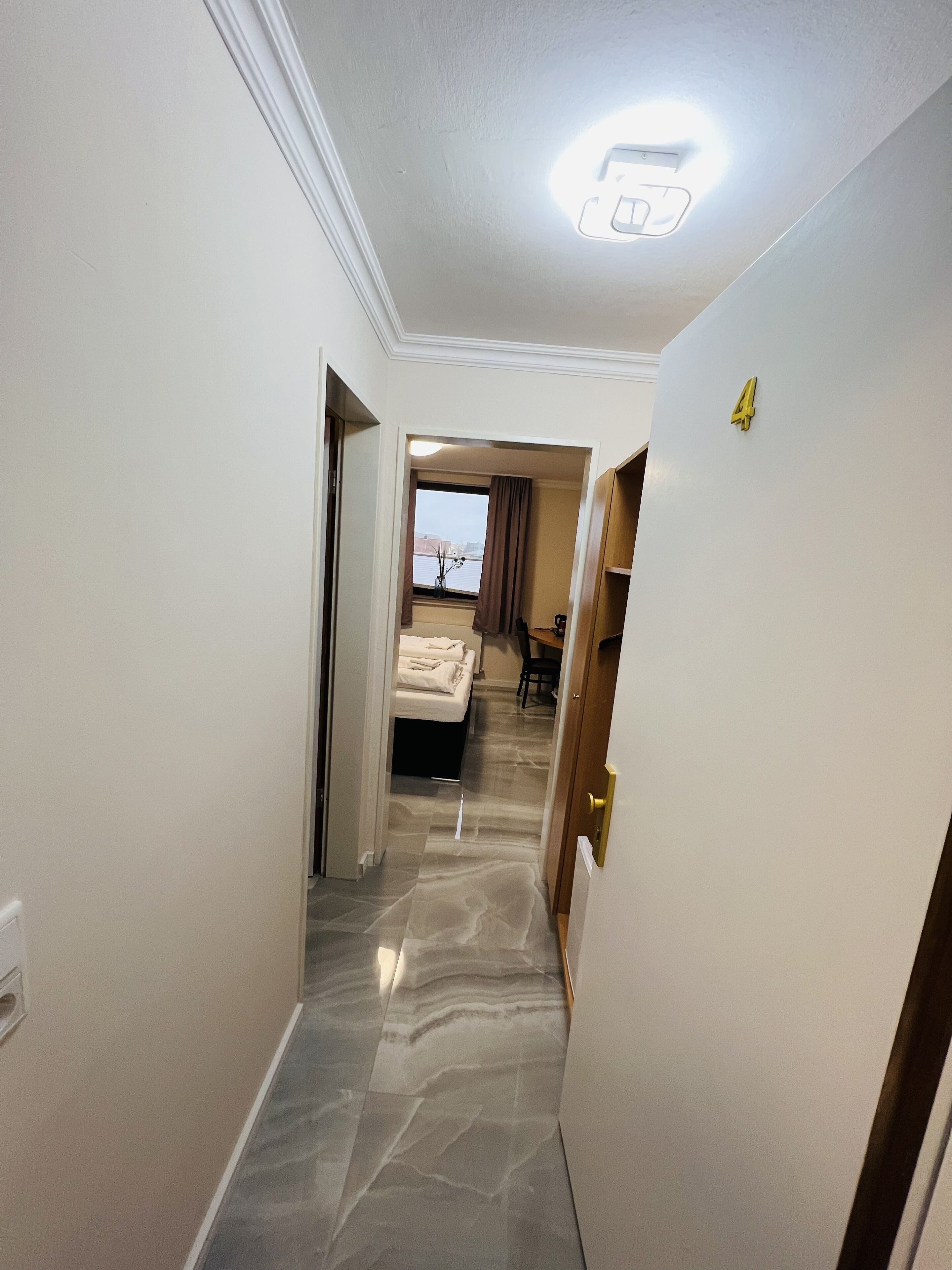 Un pasillo de hotel con piso de mármol, una cama al fondo y una puerta con el número 4.
