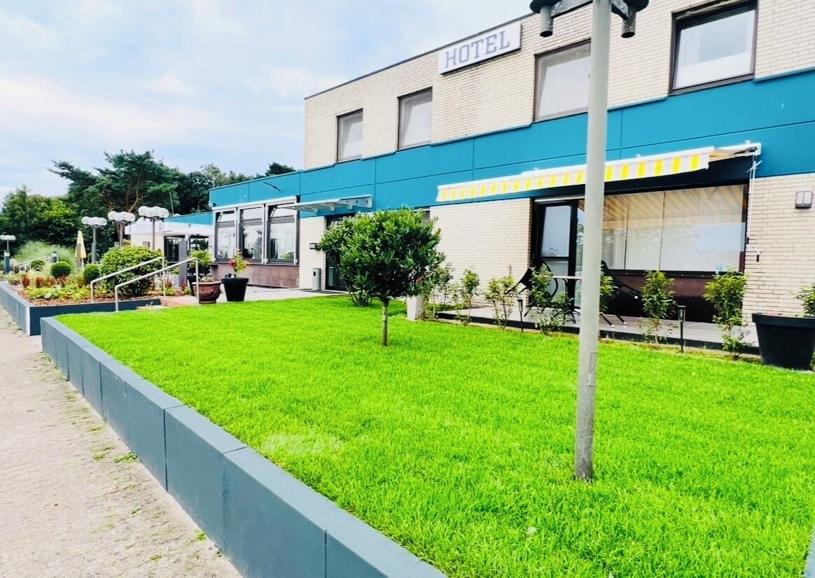 A hotel with a blue awning, a grassy lawn, and a pathway leading to the entrance.
